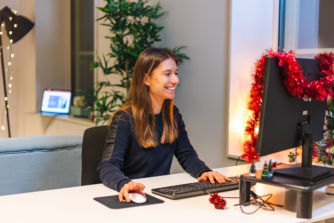 Woman working in the office smiling infront of a Christmas decorated computer screen 